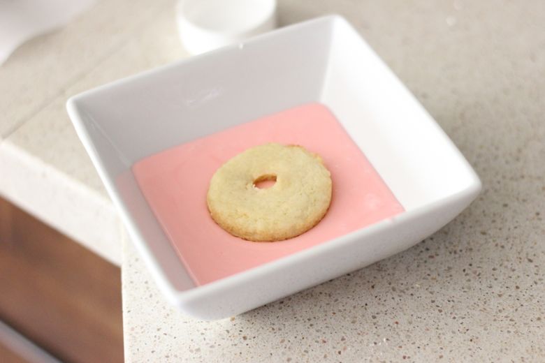 Top of Sugar Cookie Donut in a bowl of pink almond glaze.