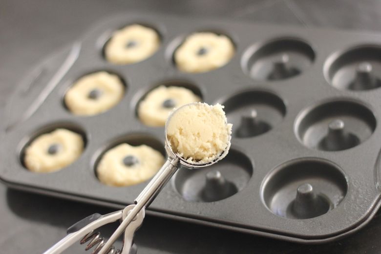 Sugar Cookie Donut dough in a cookie scoop with donut mold in the background.