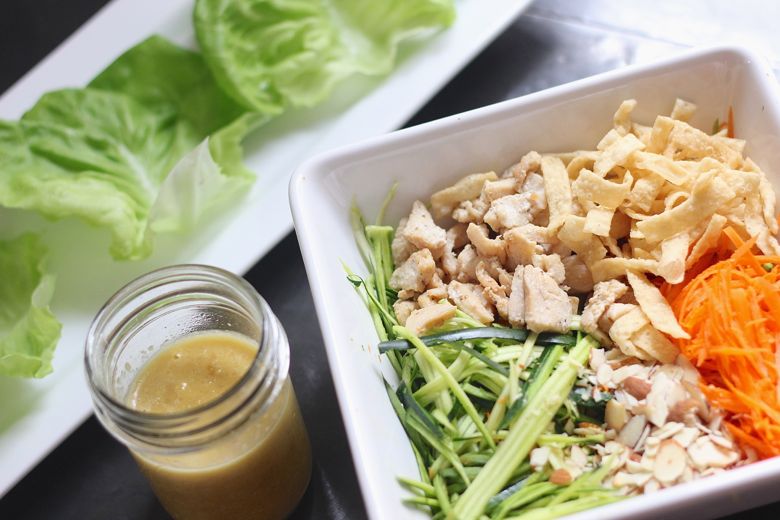 Asian Chicken Veggie Wrap filling ingredients in a large bowl with a jar of dressing and a plate of butter lettuce leaves.