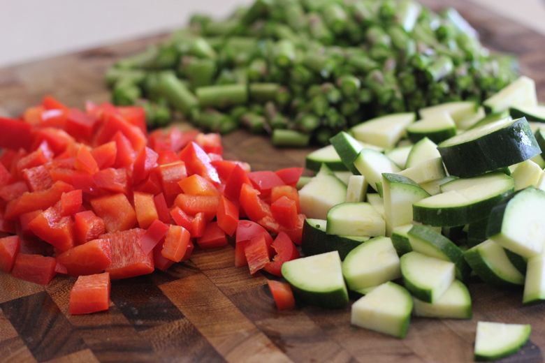 Chopped zucchini, red peppers and asparagus on a cutting board.  