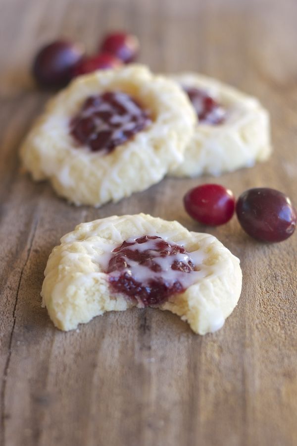 Three Cranberry Thumbprint Cookies With Almond Glaze on a board with cranberries and a bite taken out of one cookie.