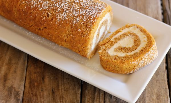 Pumpkin Roll With Maple Cream Cheese Filling on a serving plate with one piece sliced off the end.  