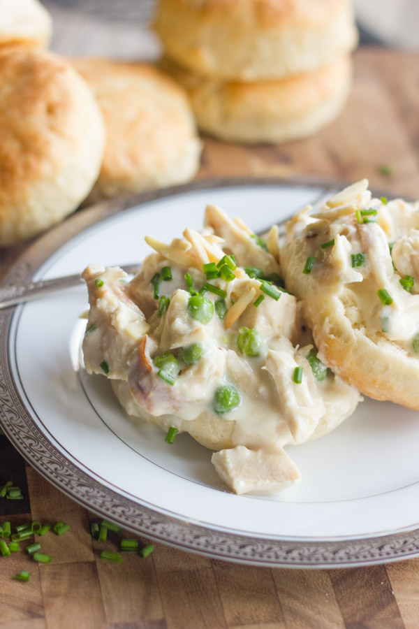Chicken a la King served on top of a biscuit sliced open on a plate, with more biscuits in the background.