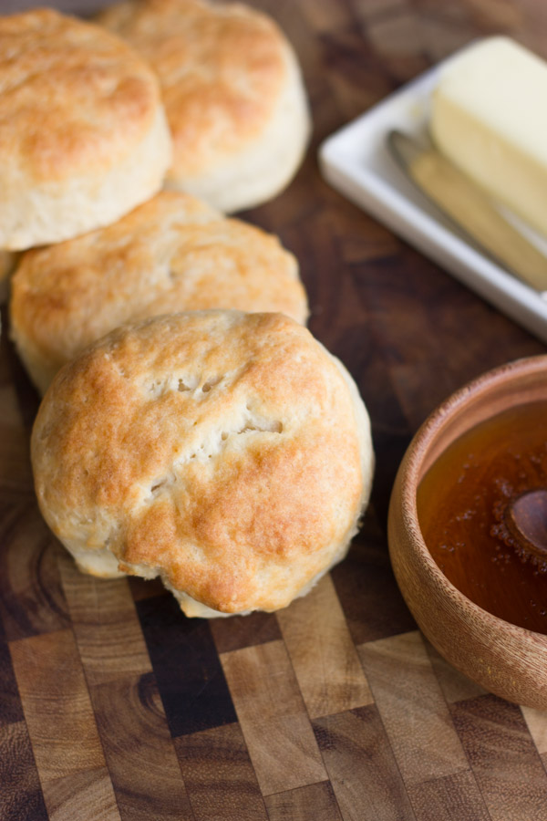 Greek Yogurt Biscuits stacked on a board with a bowl of honey and a butter dish next to them.