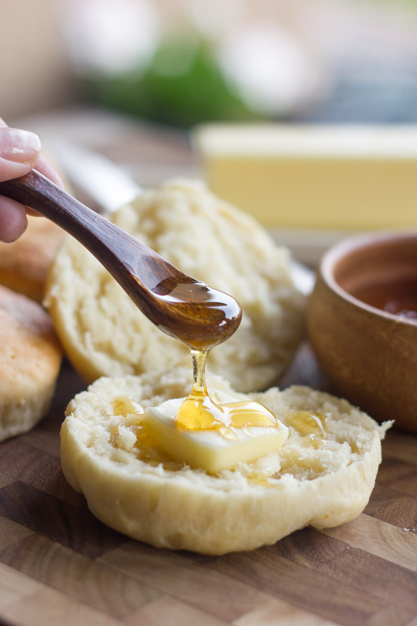 Healthier Greek Yogurt Biscuit sliced in half with a pad of butter on it and honey being drizzled on top with at little spoon.