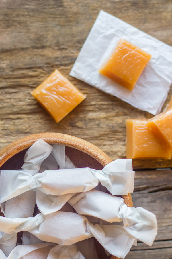 Homemade Soft Caramels wrapped in parchment paper in a bowl with some Homemade Soft Caramel squares next to the bowl.  