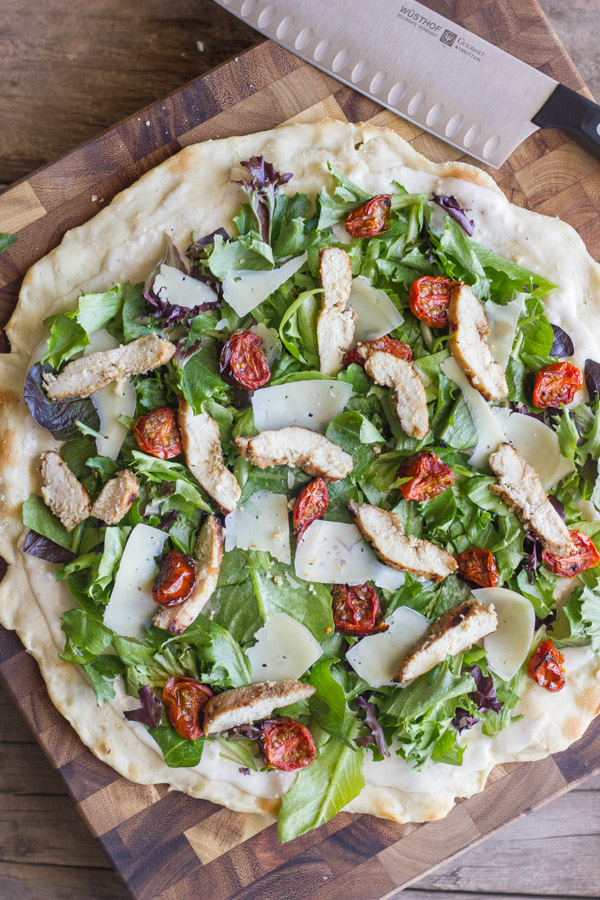 Chicken Caesar Pizza With Oven Roasted Tomatoes on a cutting board with a knife.