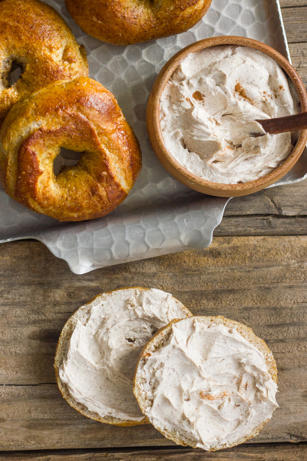Whole Wheat Soft Pretzel Bagel sliced in half with Cinnamon Sugar Cream Cheese spread on it, and a serving platter of bagels and cream cheese next to it.