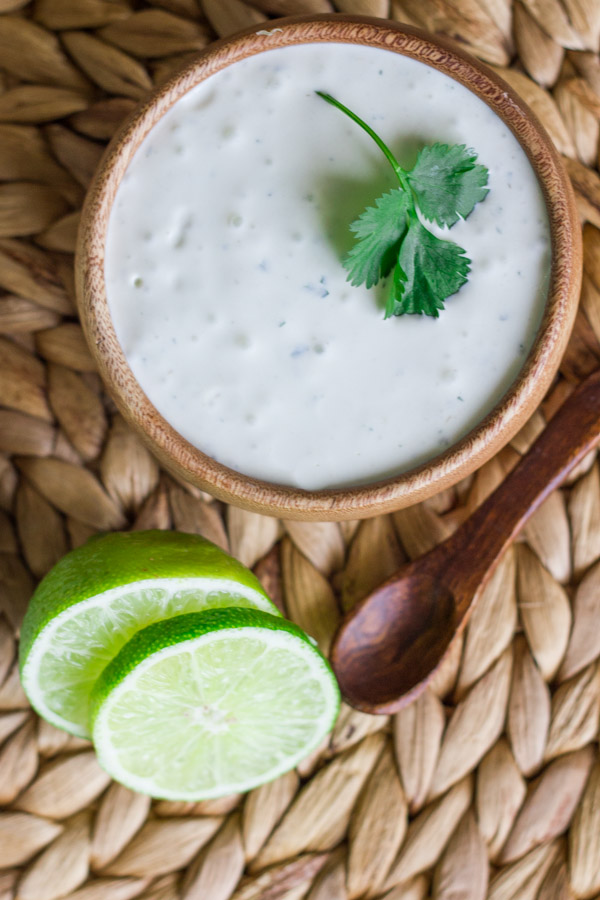 A bowl of Cilantro Lime Cream with a sliced lime and small spoon next to it.  