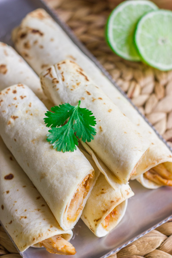 Baked Honey Lime Chicken Taquitos stacked on a serving platter, with a sliced lime in the background.  