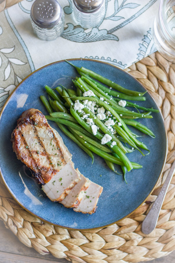 Marinated Grilled Pork Chop on a plate with green beans topped with feta.  