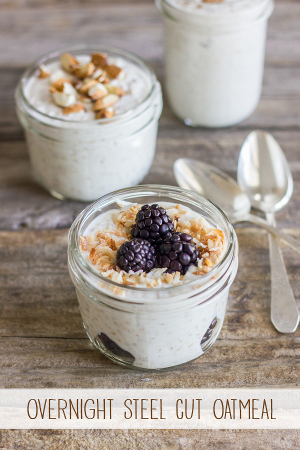 Overnight Steel Cut Oatmeal with berries and toasted coconut in a glass jar, with two other glass jars of Overnight Steel Cut Oatmeal and mix-ins in the background with two spoons. 