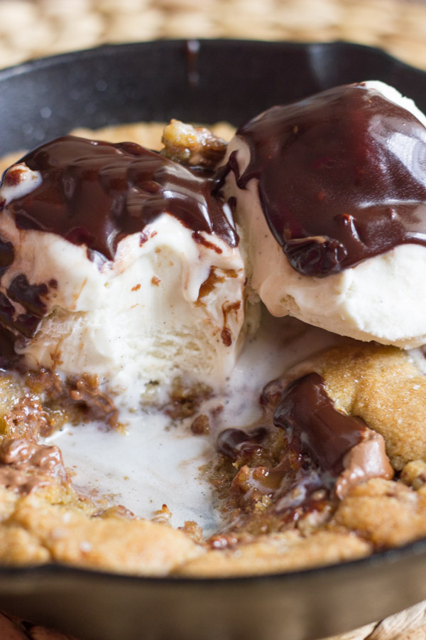 Salted Rolo Chip Pizookie in a small cast iron skillet, topped with vanilla ice cream and Homemade Hot Fudge, with some missing bites from the middle. 