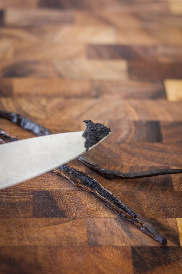 A vanilla bean pod sliced open, and knife with the vanilla caviar on the tip of it.