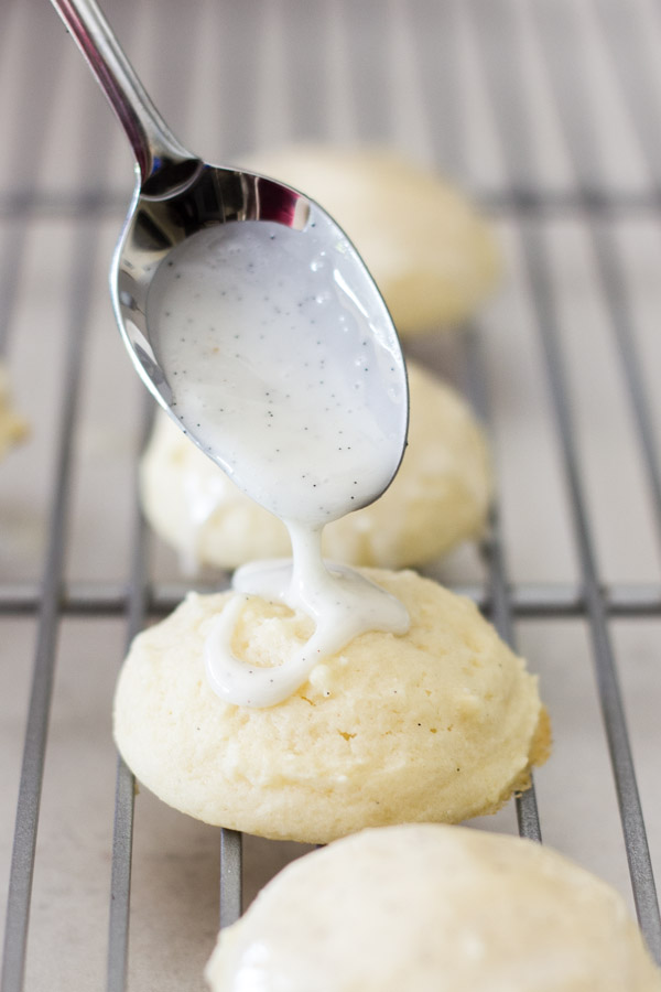 Soft Ricotta Cookies on a cooling rack, with Vanilla Bean Glaze being spooned on top of a cookie.