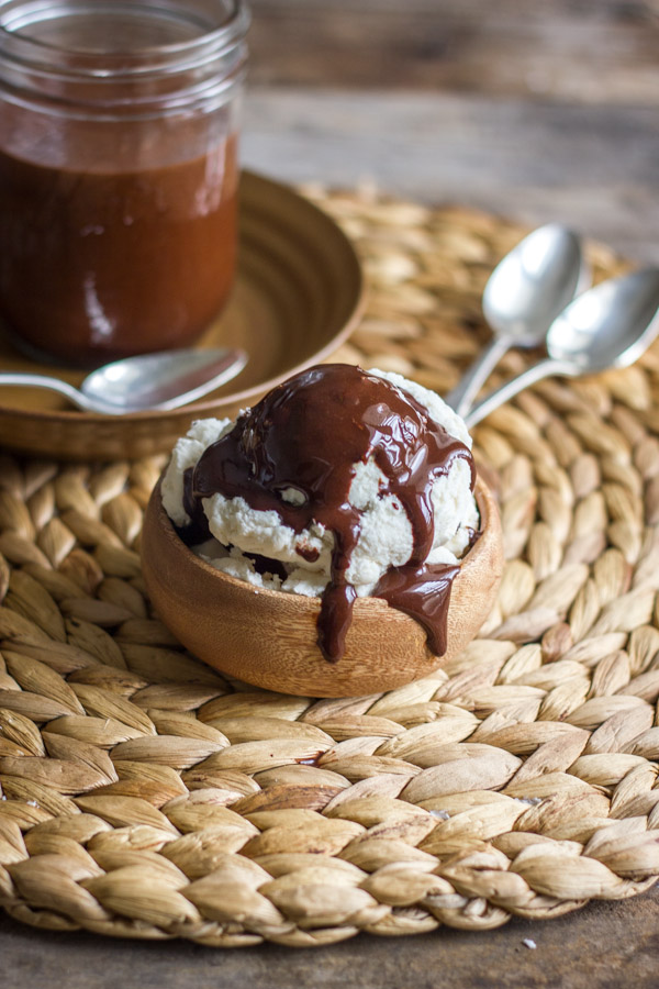 Two Ingredient All Natural Chocolate Syrup on top of vanilla ice cream in a small bowl, with a glass jar of Two Ingredient All Natural Chocolate Syrup in the background.  