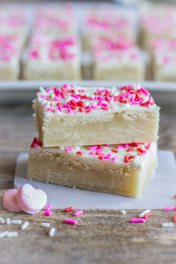Two Easy White Chocolate Sugar Cookie Bars stacked on top of each other, with sprinkles and two candy hearts near by.  