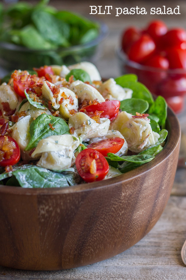 BLT Pasta Salad in a bowl, with a glass dish of spinach and a glass dish of grape tomatoes in the background.
