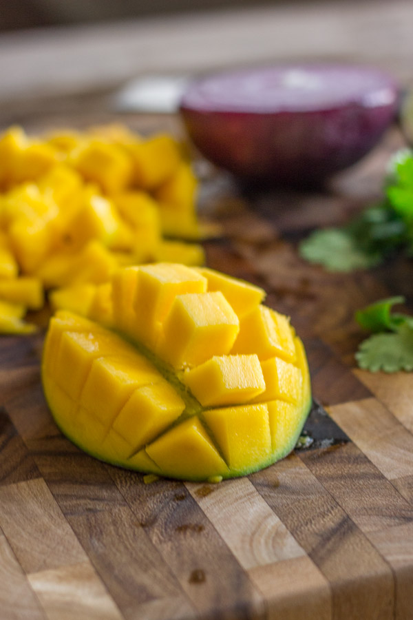 A mango diced on a cutting board, with a half red onion and cilantro in the background. 
