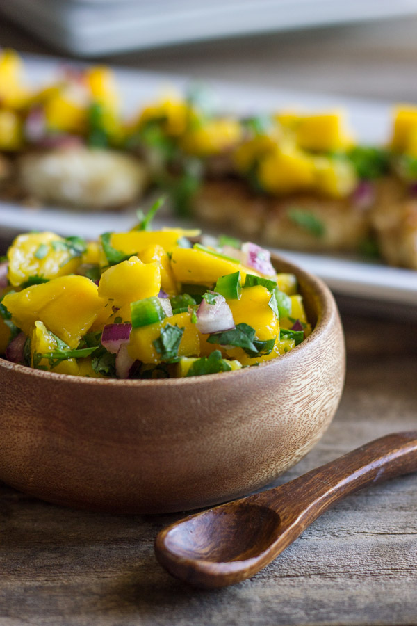 A bowl of Mango Salsa, and Coconut Crusted Chicken With Mango Salsa on top, on a serving plate in the background.  
