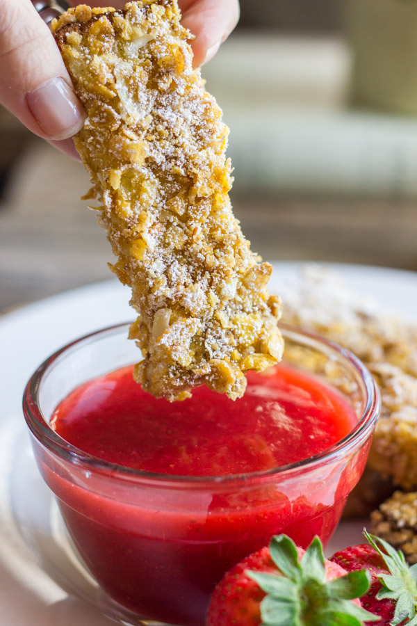 Crunchy Baked French Toast Stick being dipped into a glass dish of Strawberry Syrup.  