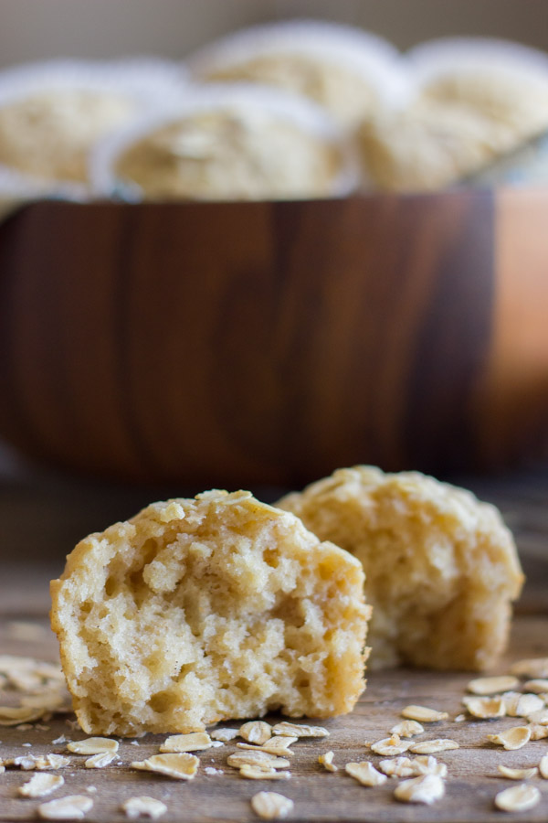 Healthy Applesauce Oat Muffin halved with oats sprinkled around it, and more muffins in a large bowl in the background.   