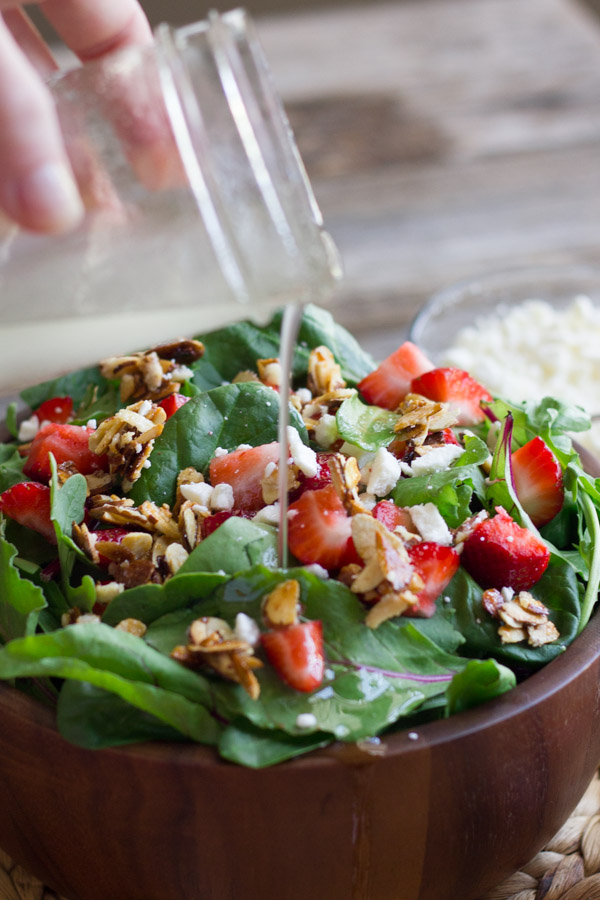 Strawberry and Spinach Salad in a bowl with a glass jar of Almond Vinaigrette being poured on top.