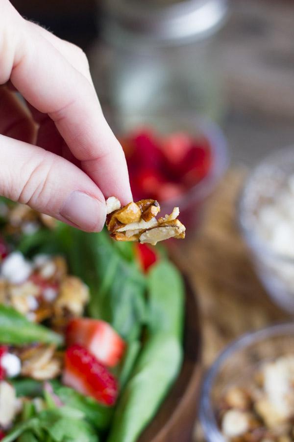 A sugared almond, with a bowl of Strawberry and Spinach Salad with Almond Vinaigrette and salad ingredients in the background.