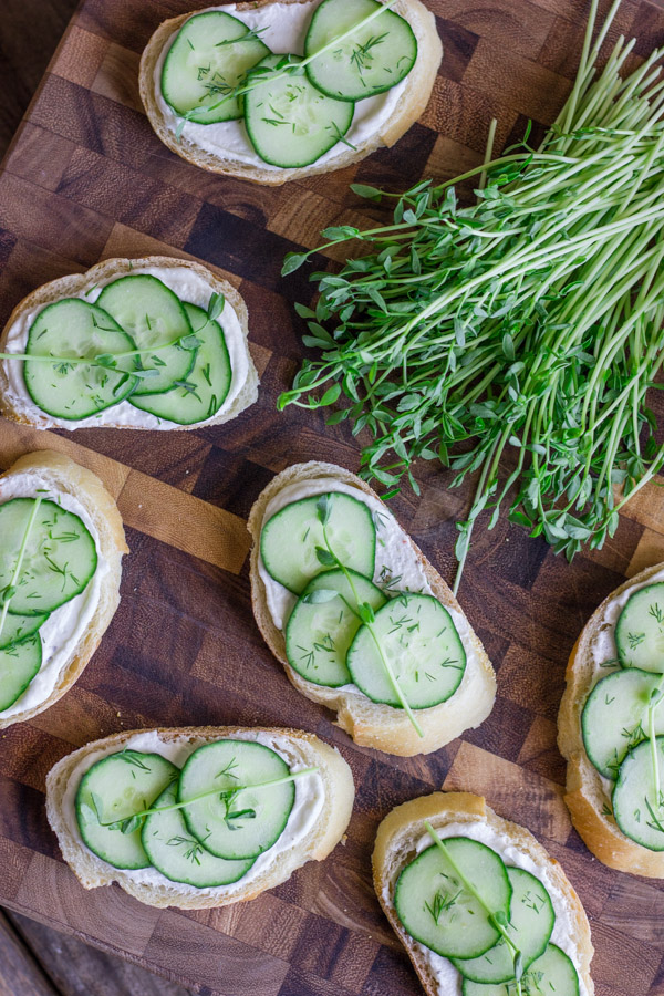 Cucumber Sandwiches With Whipped Goat Cheese on a cutting board with a bundle of pea shoots.  