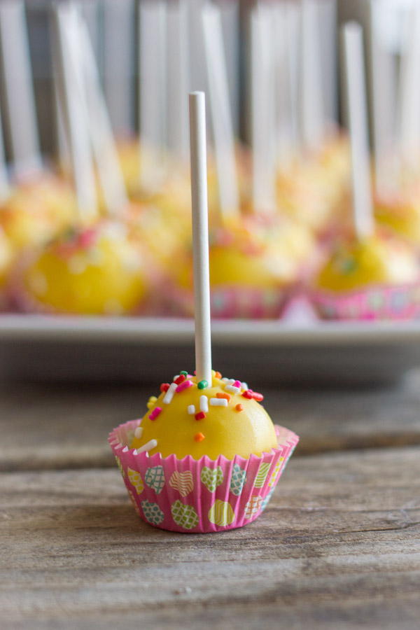 Easy Donut Hole Cake Pop in a mini muffin liner, with a platter of more cake pops in the background.
