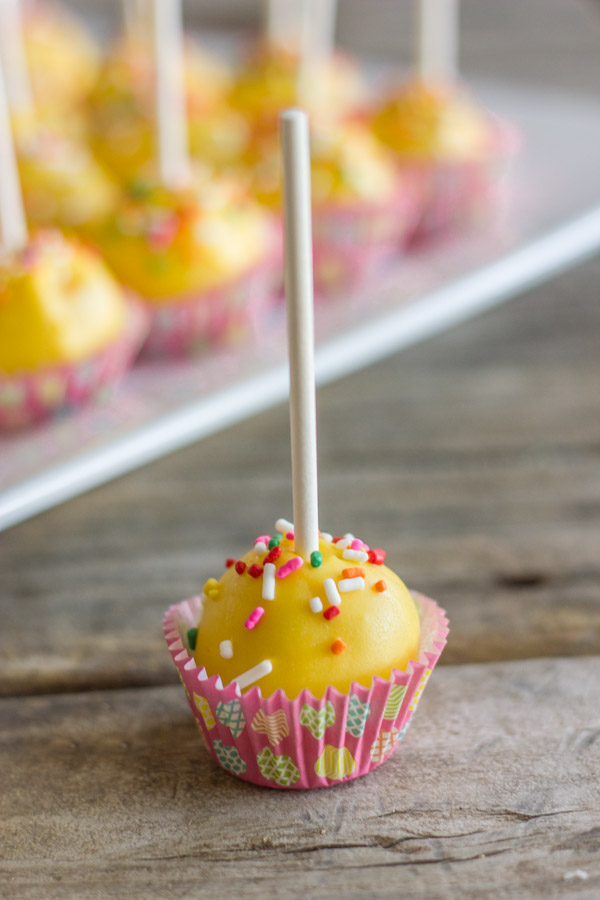 Easy Donut Hole Cake Pop in a mini muffin liner, with a platter of more cake pops in the background.