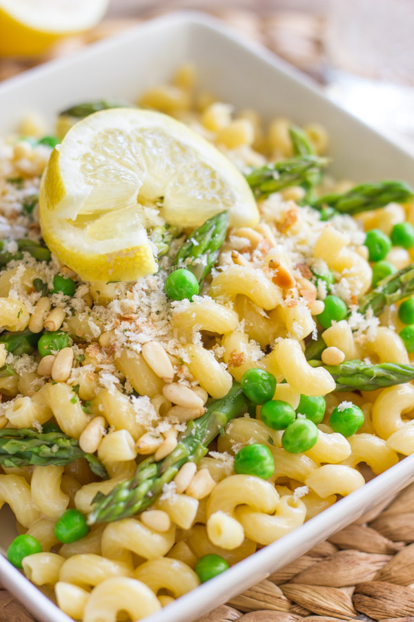 Springtime Pasta With Brown Butter Garlic Cream Sauce in a square bowl, topped with homemade breadcrumbs and a lemon wedge.