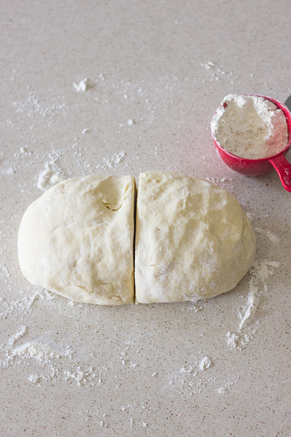 The Best Butterhorn Rolls dough divided into two equal parts, with a measuring cup of flour in the background.  