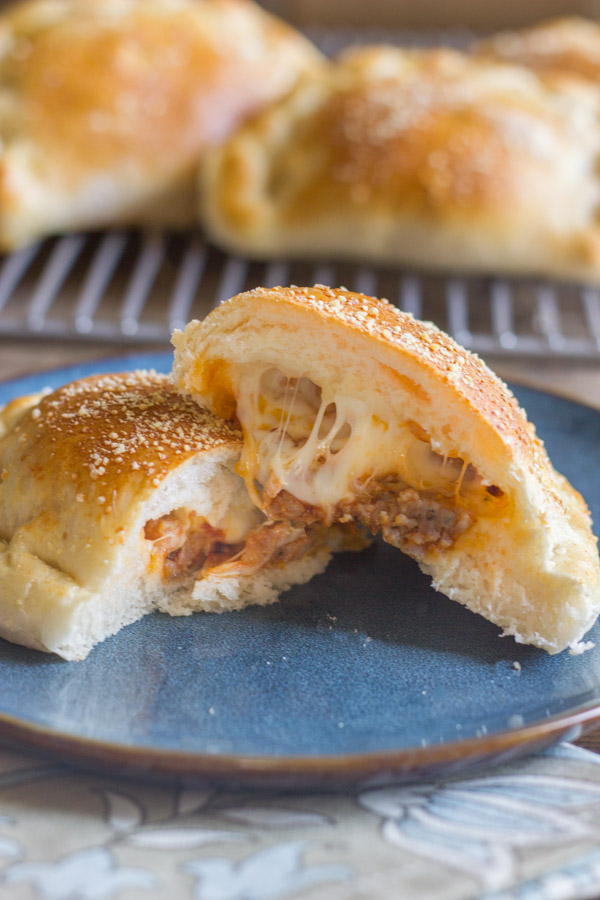 Homemade Calzone With Italian Sausage And Mozzarella cut in half on a plate, with more calzones on a cooling rack in the background.  
