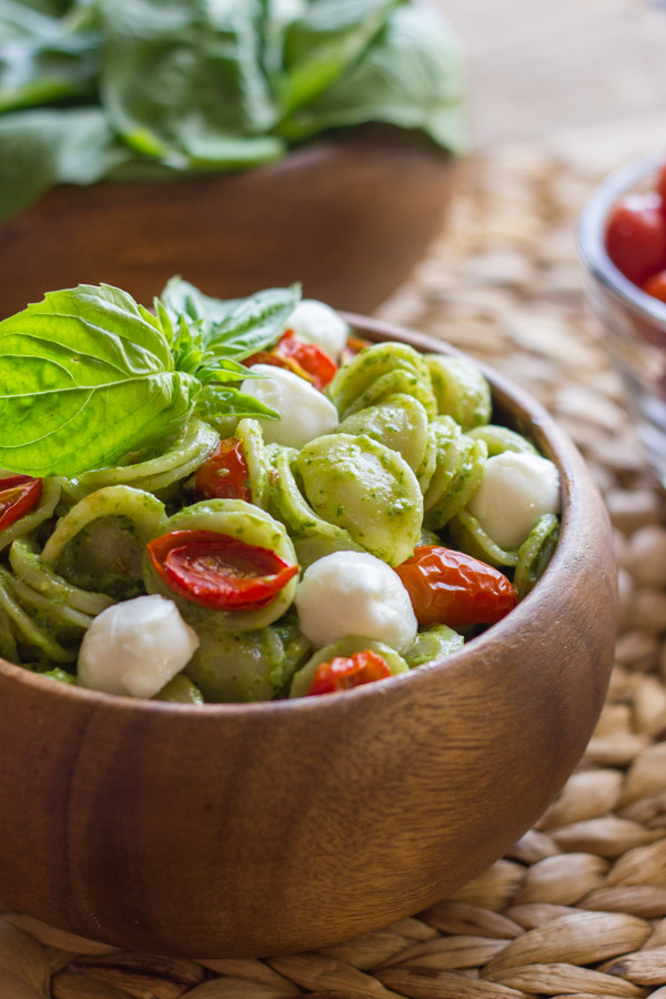 Orecchiette With Pesto and Oven Roasted Tomatoes in a bowl, topped with fresh basil leaves.
