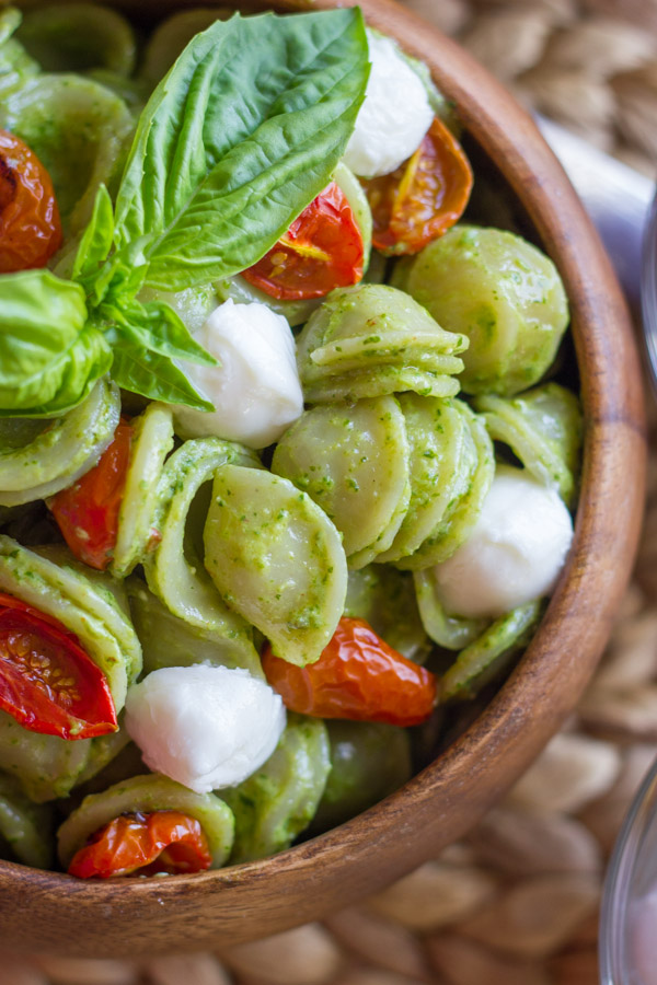Orecchiette With Pesto and Oven Roasted Tomatoes in a bowl, topped with fresh basil leaves.