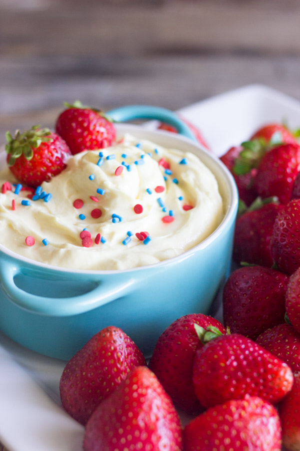 Easy Creamy Vanilla Pudding Fruit Dip in a bowl topped with sprinkles and fresh strawberries, surrounded by more fresh strawberries on a platter.