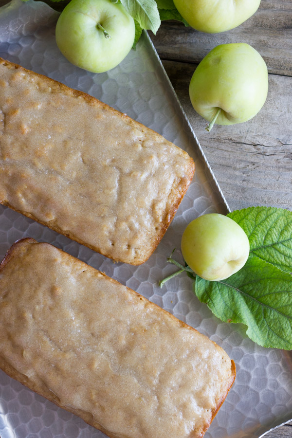 Glazed Apple Cinnamon Oatmeal Bread loaves on a serving platter, with whole apples next to them.
