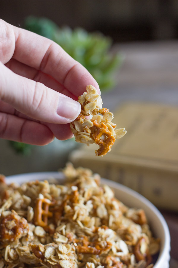 Pretzel Granola Made With Coconut Oil in a bowl, with a clump of granola being held above the bowl.