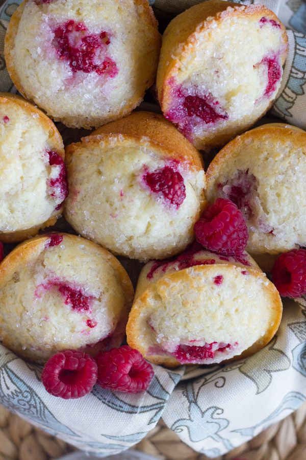 Healthier Raspberry Almond Muffins in a cloth lined bowl with a few fresh raspberries.