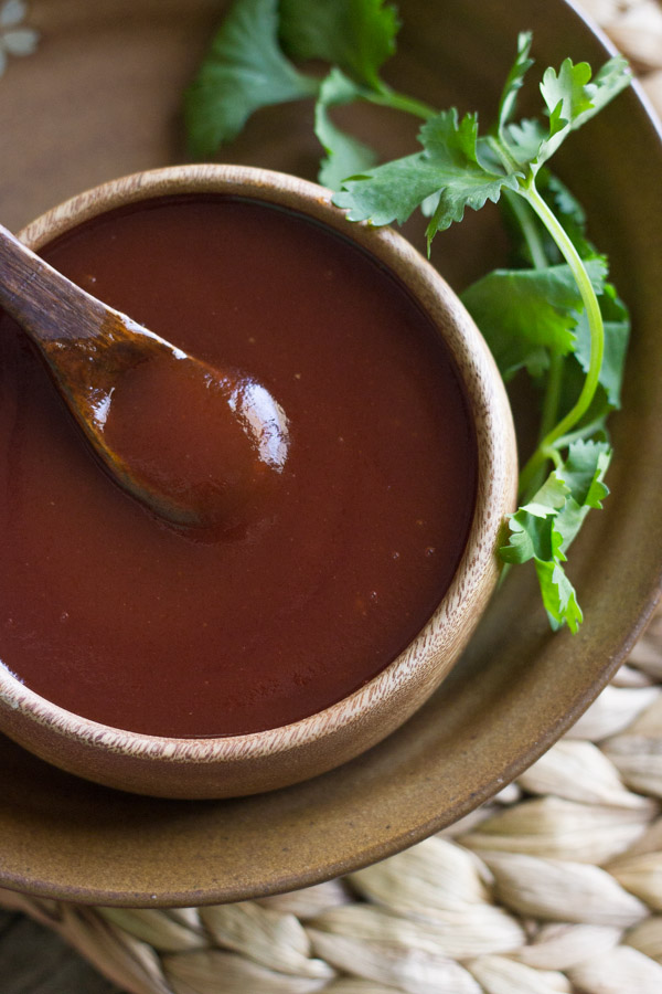 Homemade Honey BBQ Sauce in a small wood bowl, with a small wooden spoon dipped in it, with some green garnish next to it.
