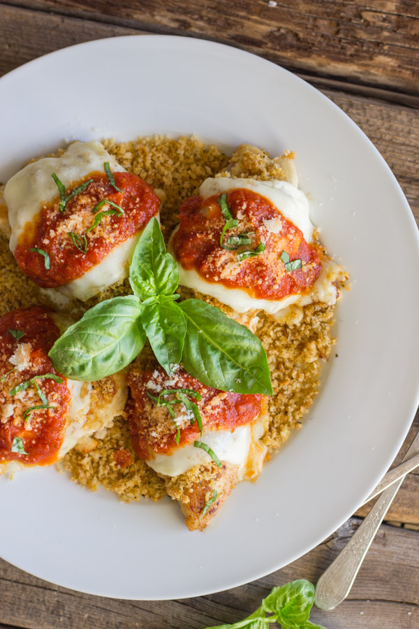 Easy Chicken Parmesan With Toasted Panko on top of a thin layer of the toasted Panko on a serving plate, topped with red sauce, grated Parmesan and some thinly sliced fresh basil, with fresh basil leaves in the center of the serving plate.  