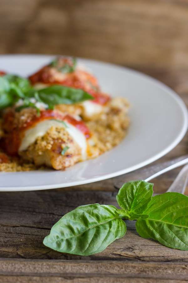 Easy Chicken Parmesan With Toasted Panko on top of a thin layer of the toasted Panko on a serving plate, topped with red sauce, grated Parmesan and some thinly sliced fresh basil, with fresh basil leaves in the center of the serving plate, and more fresh basil leaves next to the plate with some silverwear.  