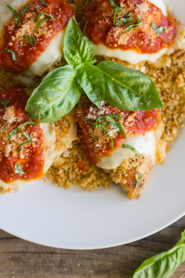 Easy Chicken Parmesan With Toasted Panko on top of a thin layer of the toasted Panko on a serving plate, topped with red sauce, grated Parmesan and some thinly sliced fresh basil, with fresh basil leaves in the center of the serving plate.  