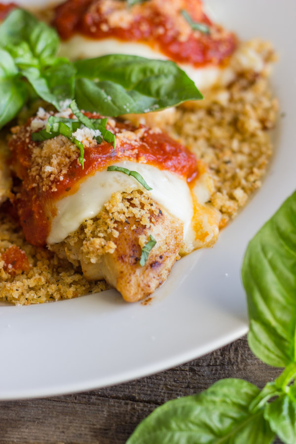 Easy Chicken Parmesan With Toasted Panko on top of a thin layer of the toasted Panko on a serving plate, topped with red sauce, grated Parmesan and some thinly sliced fresh basil, with fresh basil leaves in the center of the serving plate.  
