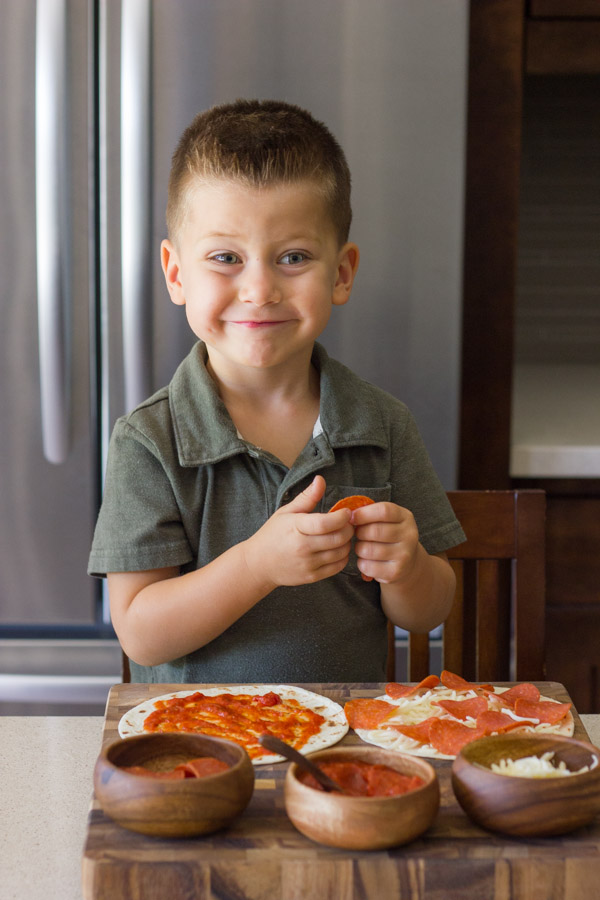 Waffled Pizza Pocket ingredients on a cutting board with a little boy assembling his pizza.