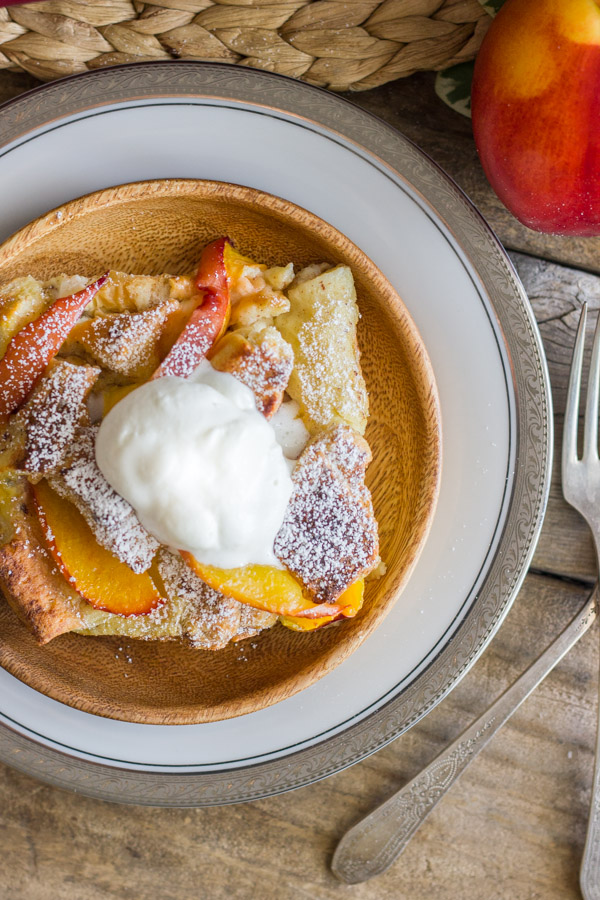 Peaches and Cream French Toast Bake topped with homemade whipped cream on a plate, with a fork and a whole peach next to it.  