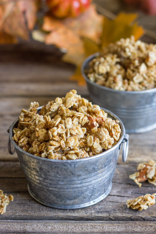 Pumpkin Pie Spice Coconut Oil Granola in two mini galvanized buckets, with some granola clusters next to the buckets and fall decorations in the background.  