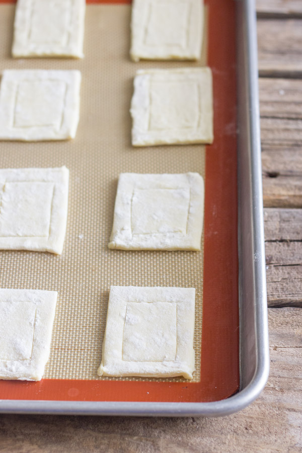 Puff pastry that has been cut and scored, arranged on a Silpat lined baking sheet. 