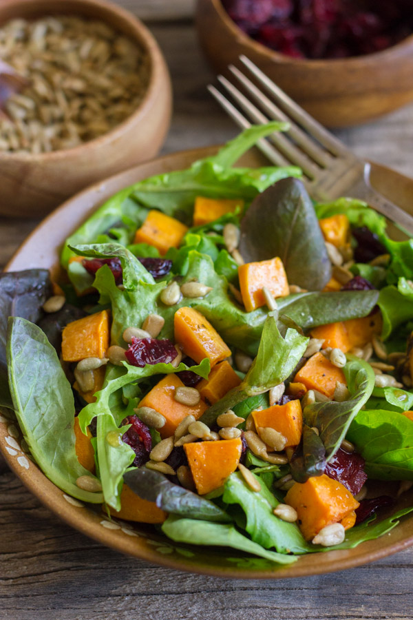 Roasted Sweet Potato Salad on a plate with a fork, with two small bowls of sunflower seeds and dried cranberries in the background.  